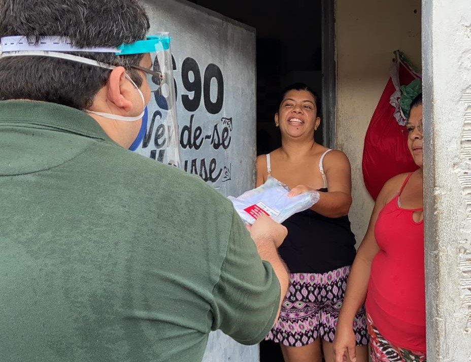 homem usando máscara entregando kit na porta de casa para duas senhoras